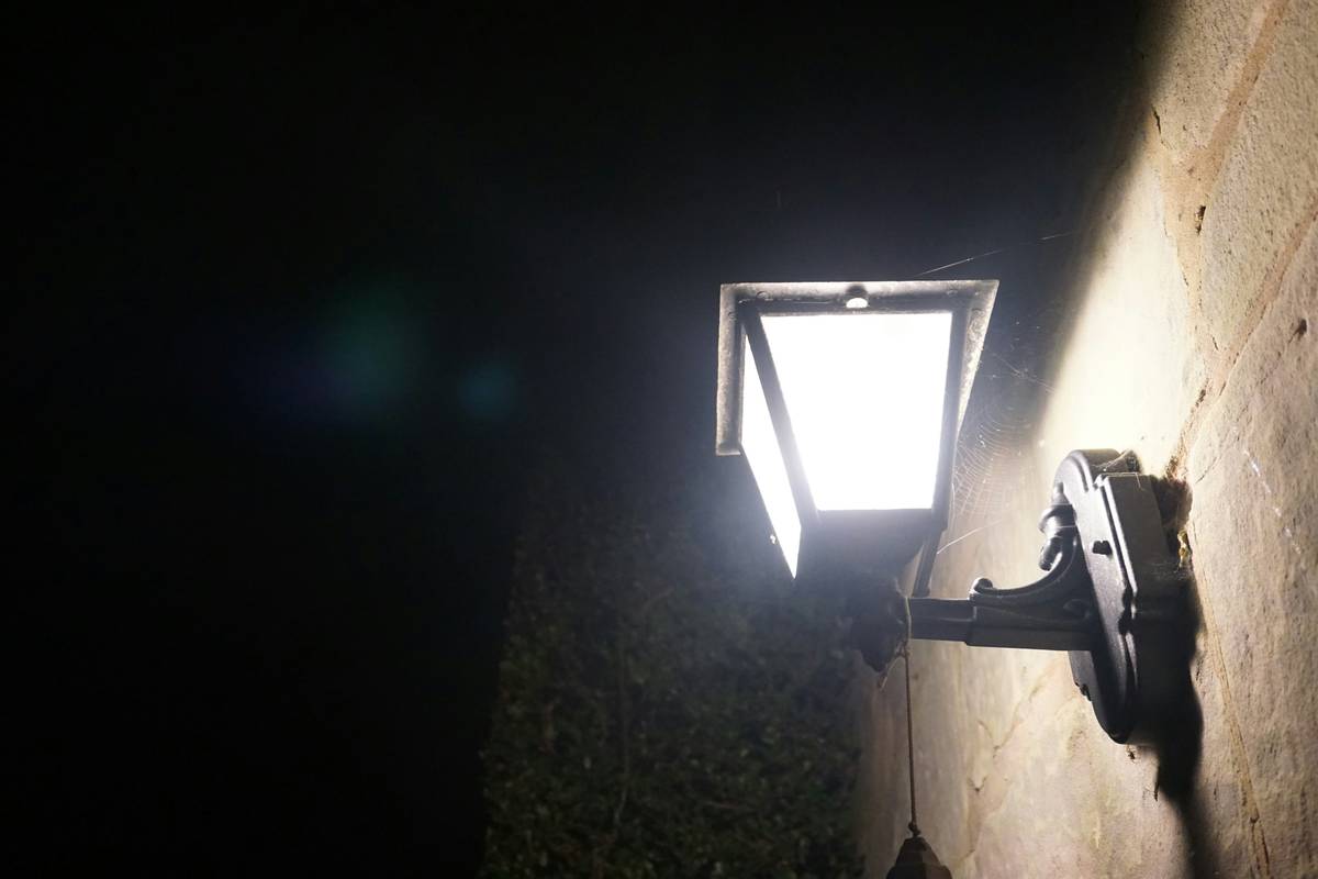 Bq outside security lights mounted on a brick garage wall with clear wiring conduit and downward-focused illumination zone